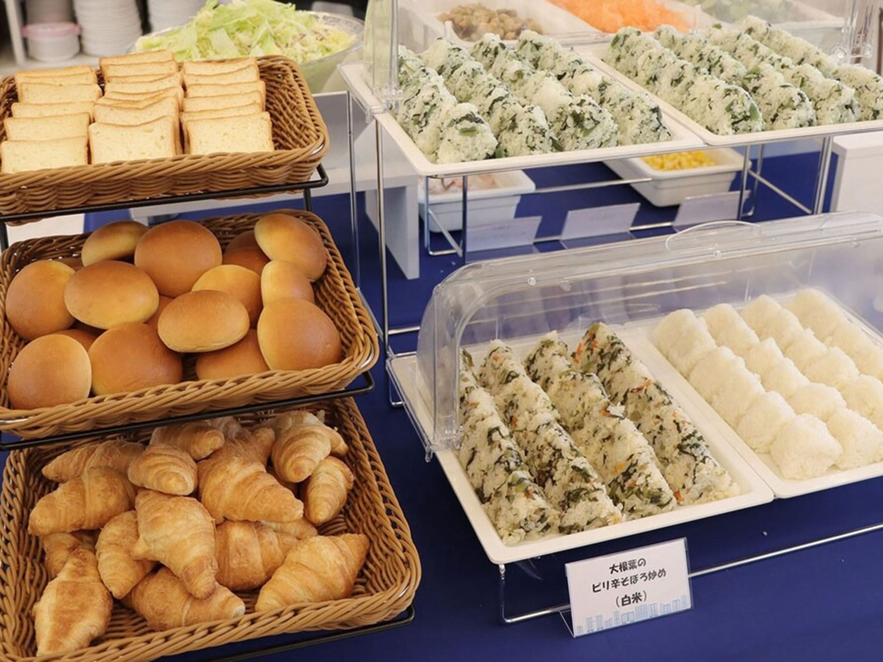 Un bufé con diversas opciones de comida, incluyendo pan, bollos, croissants y rollitos de sushi.