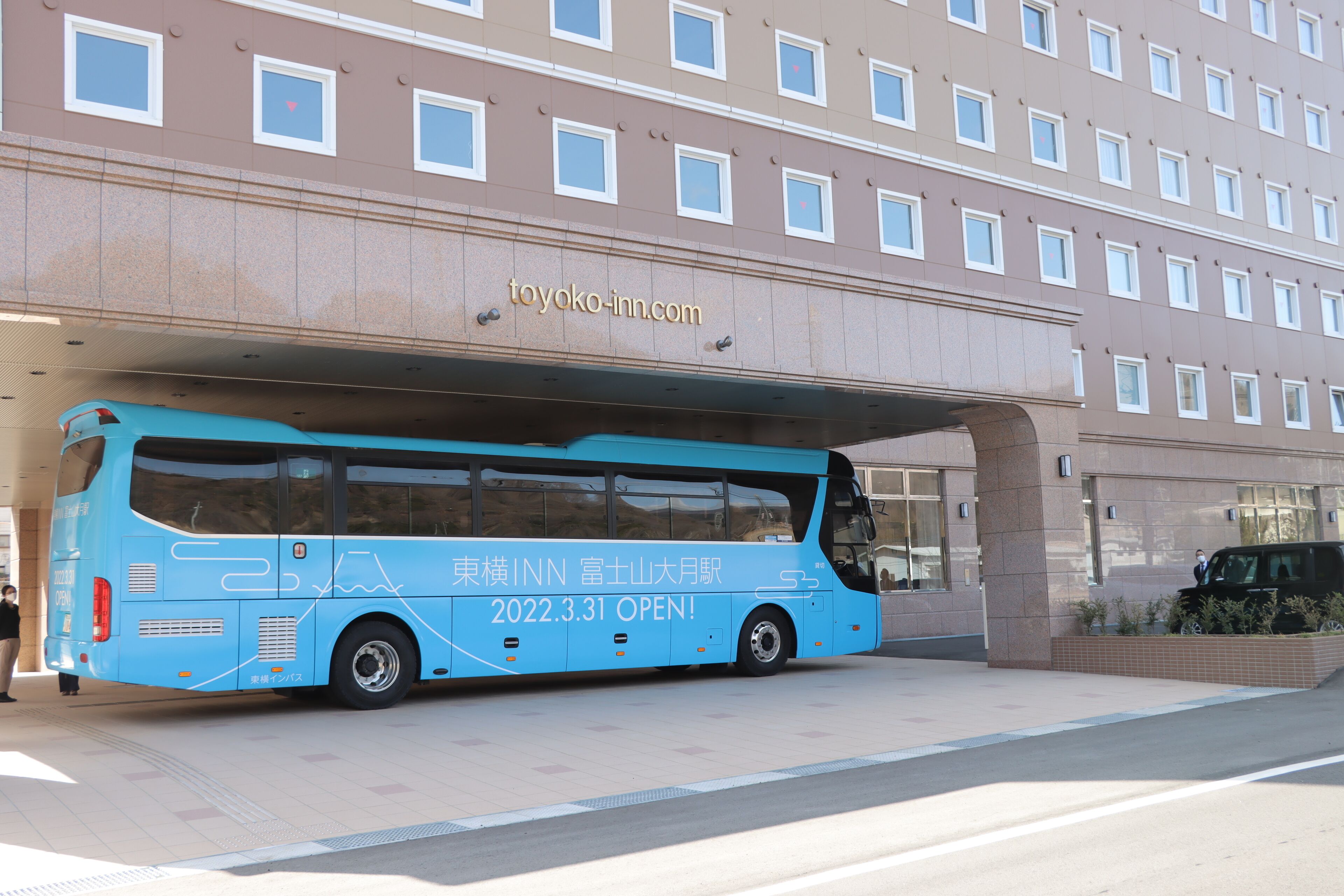 A blue bus parked in front of a building with the sign "toyoko-inn.com".