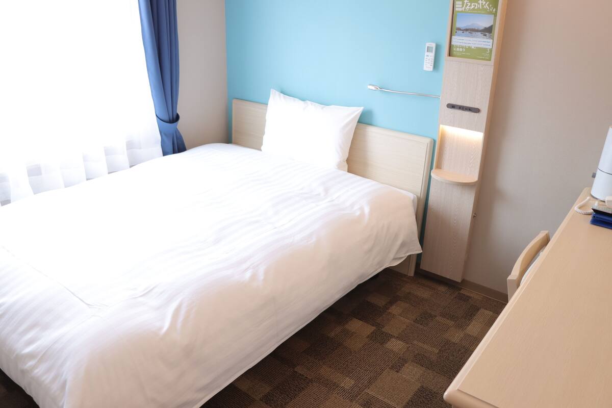Habitación de hotel con una cama, una mesita de noche, un tablero de anuncios y un teléfono en la pared.