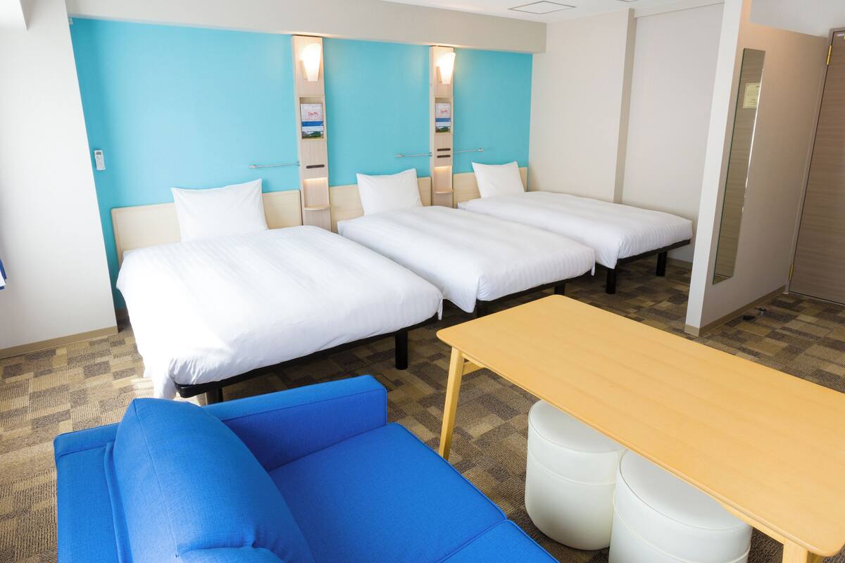 Habitación de hotel con dos camas individuales, un sofá azul, una mesa de madera y un espejo en la pared.