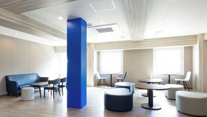 A modern hotel lobby with a blue accent wall, wooden flooring, and a mix of seating options including a blue sofa, round tables, and chairs. - Toyoko Inn Fujisan Otsuki-eki (Otsuki)
