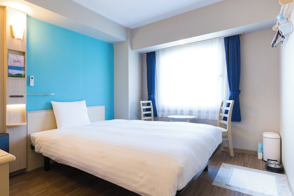 Una habitación de hotel con una cama grande, un escritorio, una silla, una mesita y una ventana con cortinas.