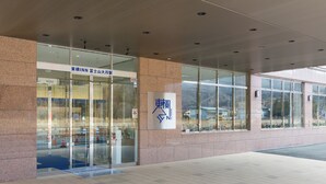 A hotel entrance with glass doors, a sign with Japanese characters, and a view of the surrounding area through the windows. - Toyoko Inn Fujisan Otsuki-eki (Otsuki)