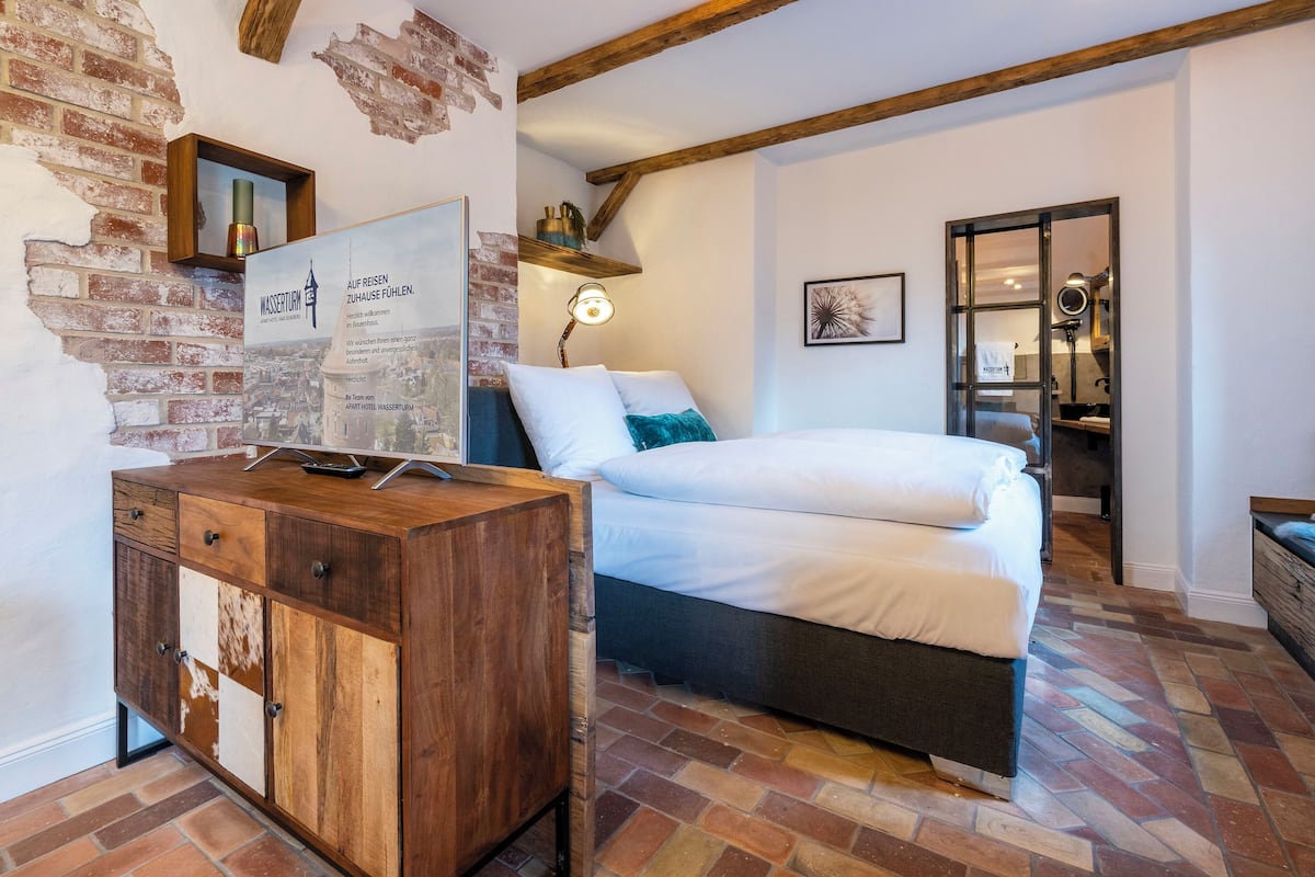 A bedroom with a bed, a wooden cabinet, a brick wall, and a framed sign.
