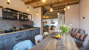 Eine moderne Küche mit Holztisch, Pendelleuchten und einem Essbereich mit einer Couch und einem Blumenstrauß.