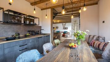 Eine moderne Küche mit Holztisch, Pendelleuchten und einem Essbereich mit einer Couch und einem Blumenstrauß.