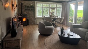 Una sala de estar moderna con chimenea, asientos cómodos y ventanas amplias con vistas a zonas verdes.