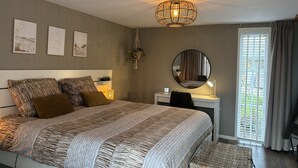 Un dormitorio con cama, mesita de noche, espejo y vistas al exterior.