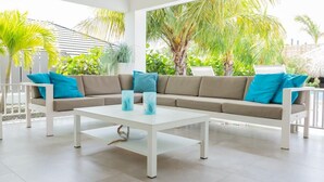 Un espacio exterior moderno con un sofá beige, cojines azules y una mesa de centro blanca.