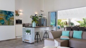 Una sala de estar moderna con sofá, mesa de centro y área de cocina con refrigerador, horno y taburetes de bar.