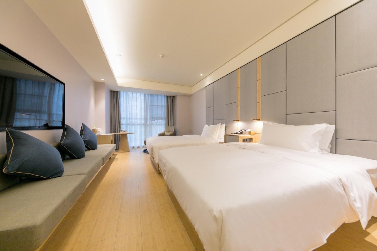 A hotel room with a large bed, a sofa, a desk, and a view of the outdoors.