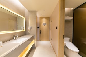 A modern bathroom with a large mirror, a sink, a toilet, and a shower area. - Ji Hotel (Heze)