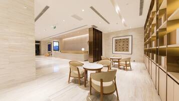 A spacious hotel lobby with a reception desk, seating area, and a wall with a framed artwork.