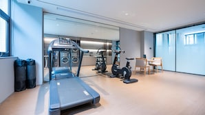 Un gimnasio moderno con cinta de correr, bicicletas estáticas y una máquina de remo. Hay una pequeña zona de descanso con una mesa y sillas.