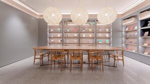 Una biblioteca moderna con una larga mesa de madera y sillas, rodeada de estanterías y tres grandes lámparas colgantes esféricas.