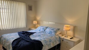 Un dormitorio con una cama, dos mesitas de noche, una lámpara, una manta y un cuadro en la pared.
