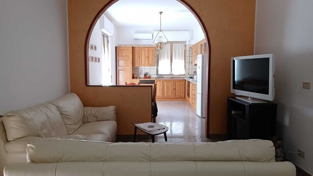 A living room with a sofa, a TV on a stand, and an archway leading to a kitchen. - House of 170 sq. m., 700 m. from the center of Rosolini (Rosolini)