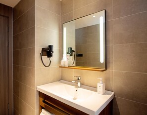 A modern bathroom with a large mirror, a white sink, and a hairdryer mounted on the wall. - Hanting Hotel (Zhengzhou)