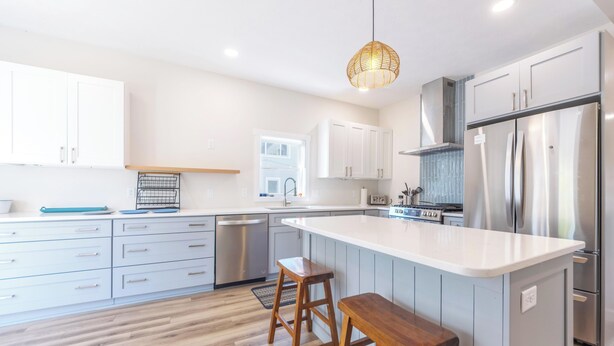 A modern kitchen with white cabinets, a large island with stools, stainless steel appliances, and a hanging light fixture. - A Liberty Haven - 2 blocks from South Beach, (South Haven)
