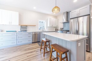 A modern kitchen with white cabinets, a large island with stools, stainless steel appliances, and a hanging light fixture. - A Liberty Haven - 2 blocks from South Beach, (South Haven)