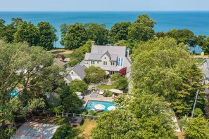 A large house with a swimming pool, surrounded by trees and a view of the ocean. - Paradise Found - Luxury Vacation- Pool, Hot tubs, Putting Green & Game Room (Fennville)