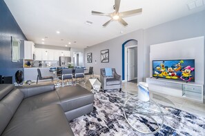 A modern living room with a grey sofa, a coffee table, and a TV displaying animated characters.