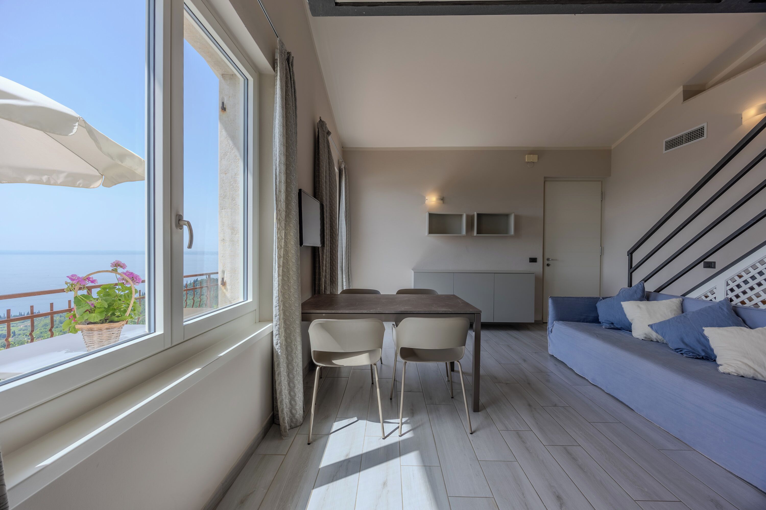 Ein modernes Wohnzimmer mit Essbereich, großen Fenstern und einem Balkon mit Meerblick.