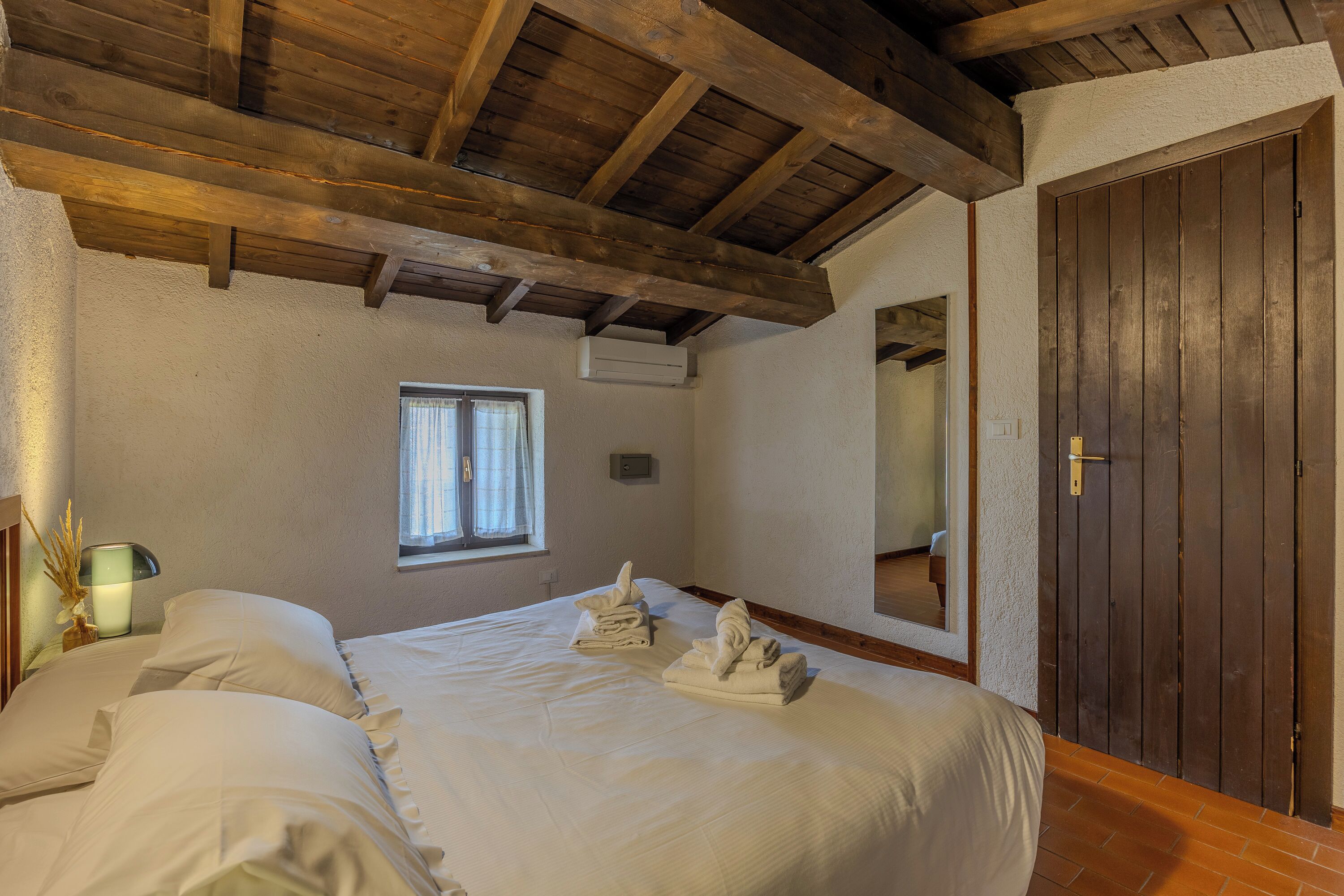 Un dormitorio con techo de madera, una cama con ropa blanca, una ventana y una puerta.