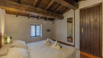 Un dormitorio con techo de madera, una cama con ropa blanca, una ventana y una puerta.