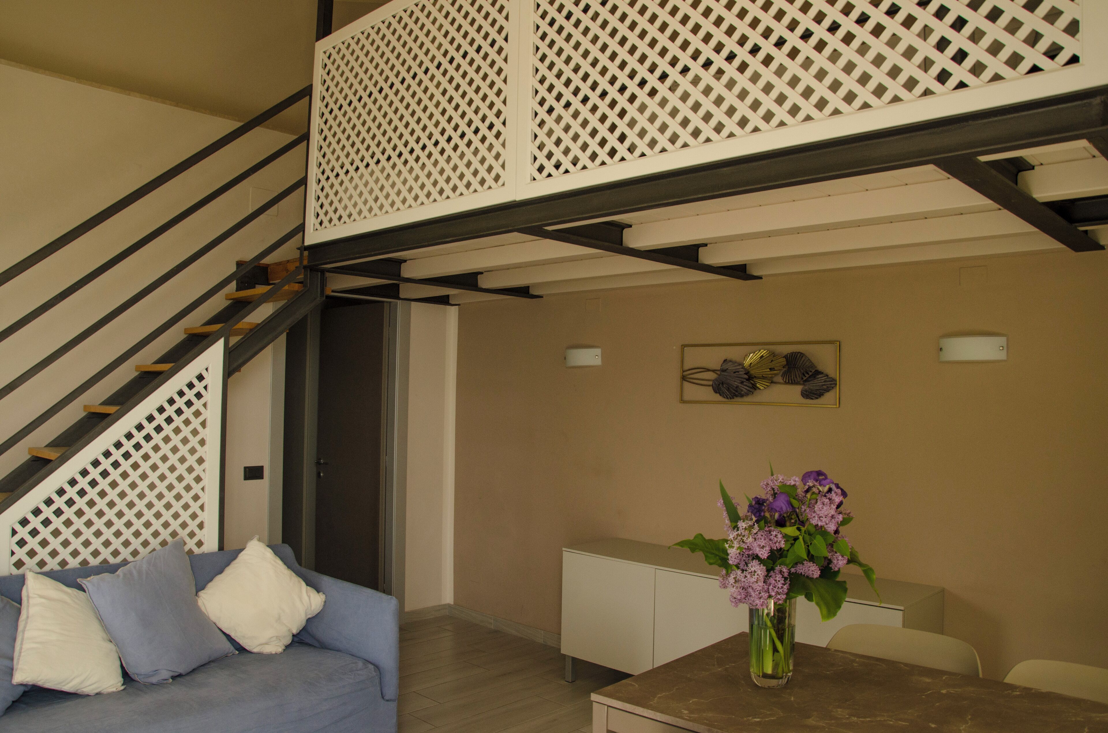Una sala de estar con una escalera, un sofá, una mesa de centro y un jarrón con flores.
