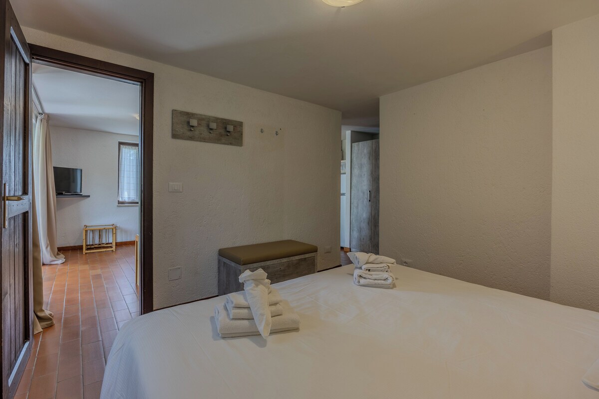 A hotel room with a bed, a bench, a television, and a window.