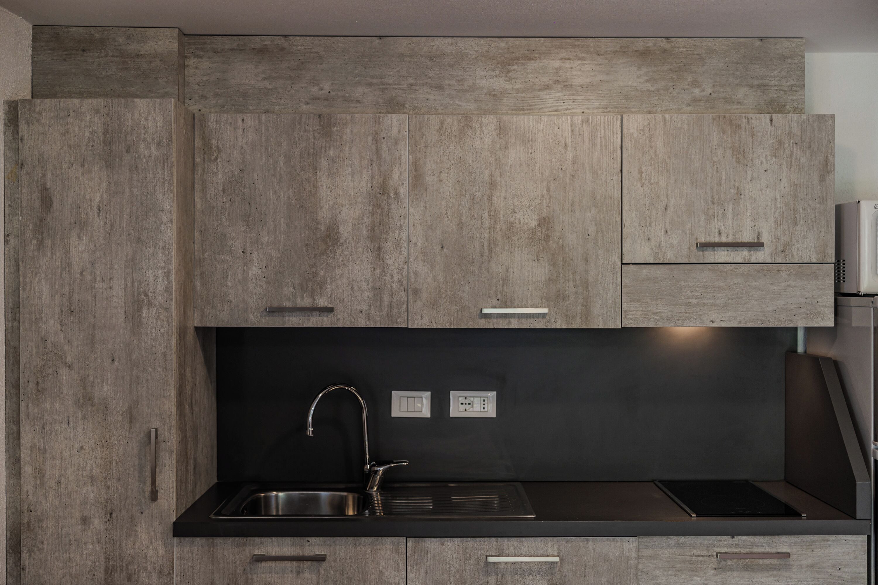 A modern kitchen with wooden cabinets, a black countertop, stainless steel sink, and a built-in stove.