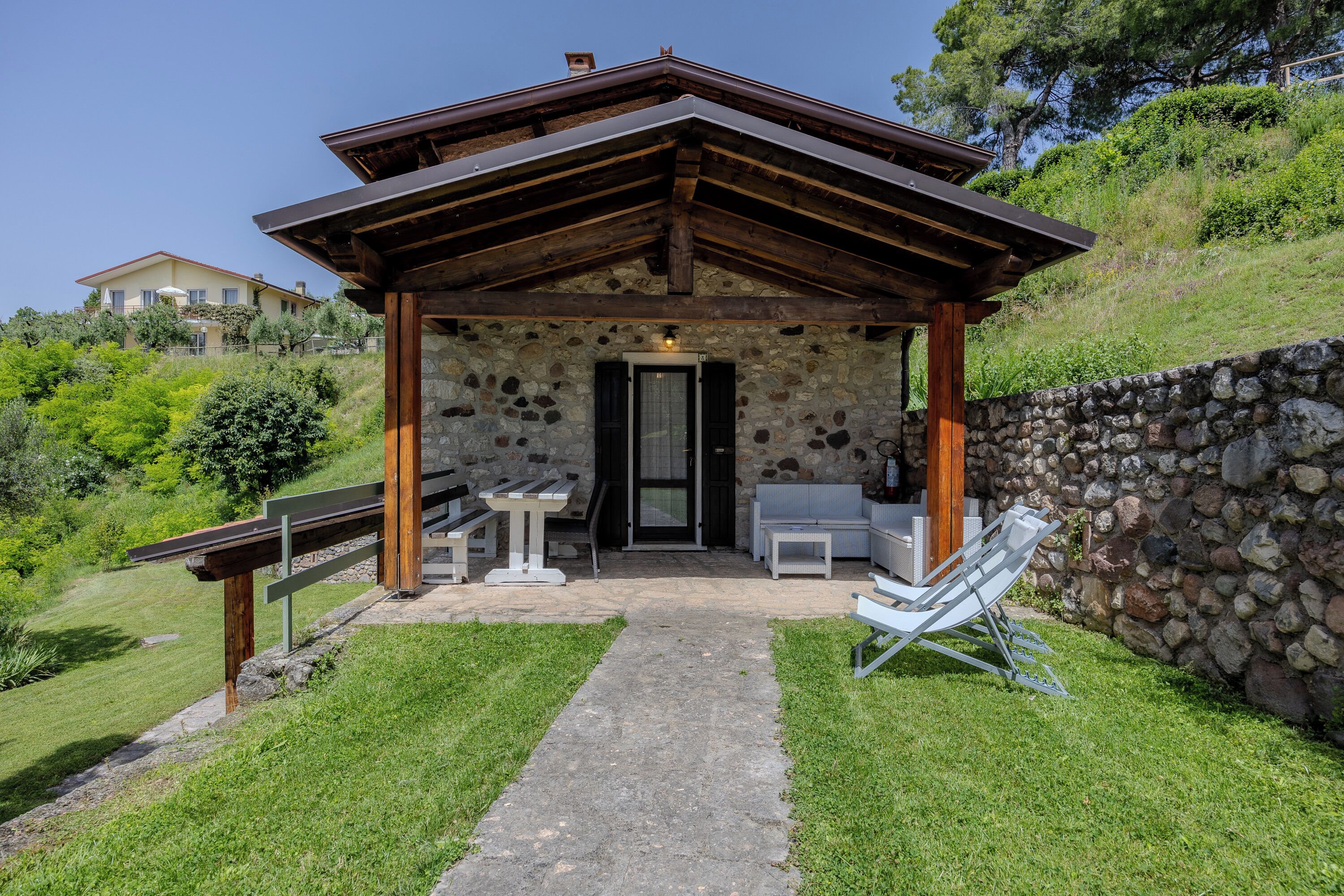 A stone building with a wooden roof, a door, and a small porch area with benches and a table.
