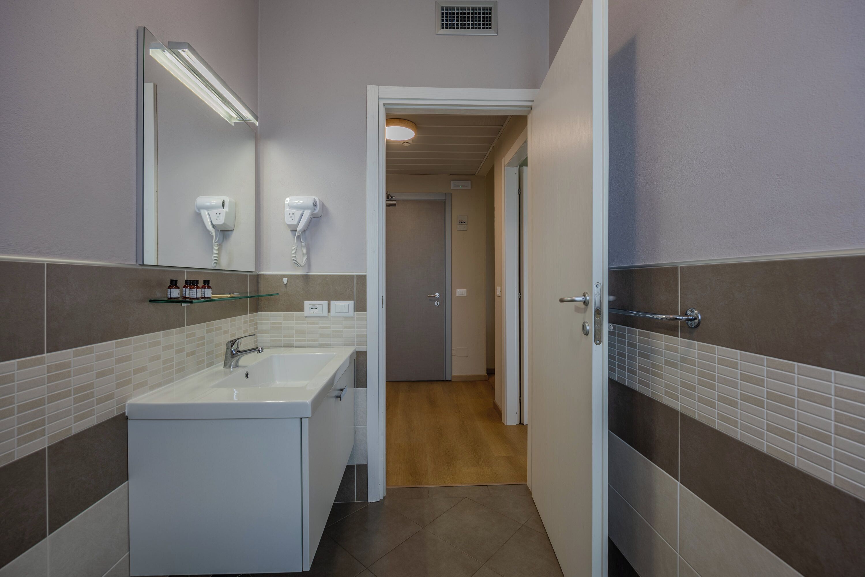 A modern bathroom with a large sink, two hair dryers, and a mirror.