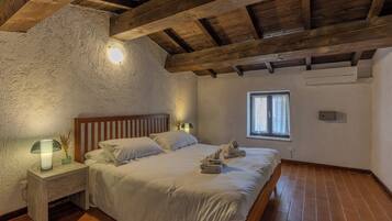 Una camera da letto con soffitto in legno, un letto con lenzuola bianche, un comodino con una lampada e una finestra vista esterna.