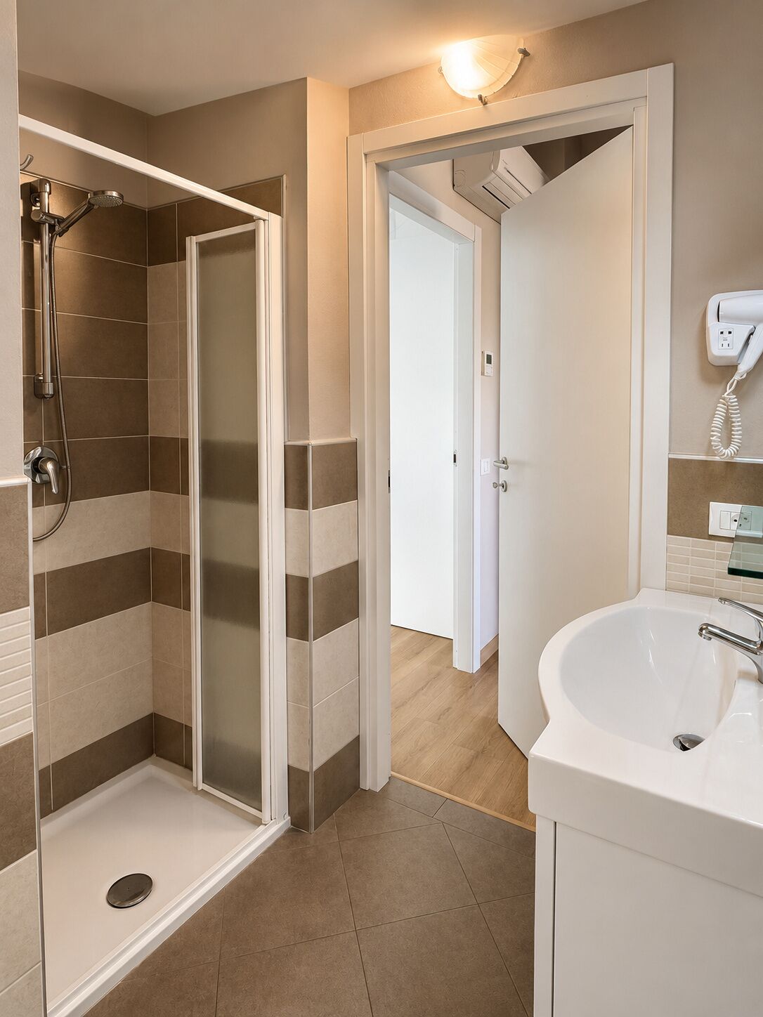 A bathroom with a shower, a sink, and a hairdryer on the wall.