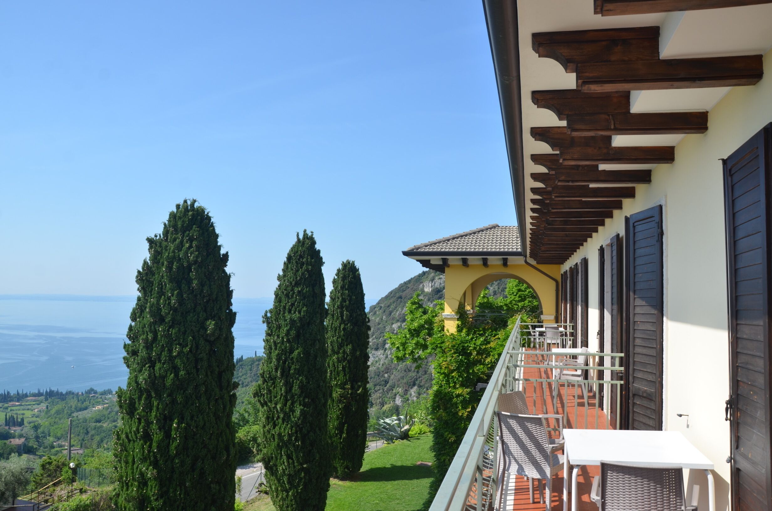 Un balcon avec vue sur la mer, de grands cyprès et une montagne en arrière-plan.