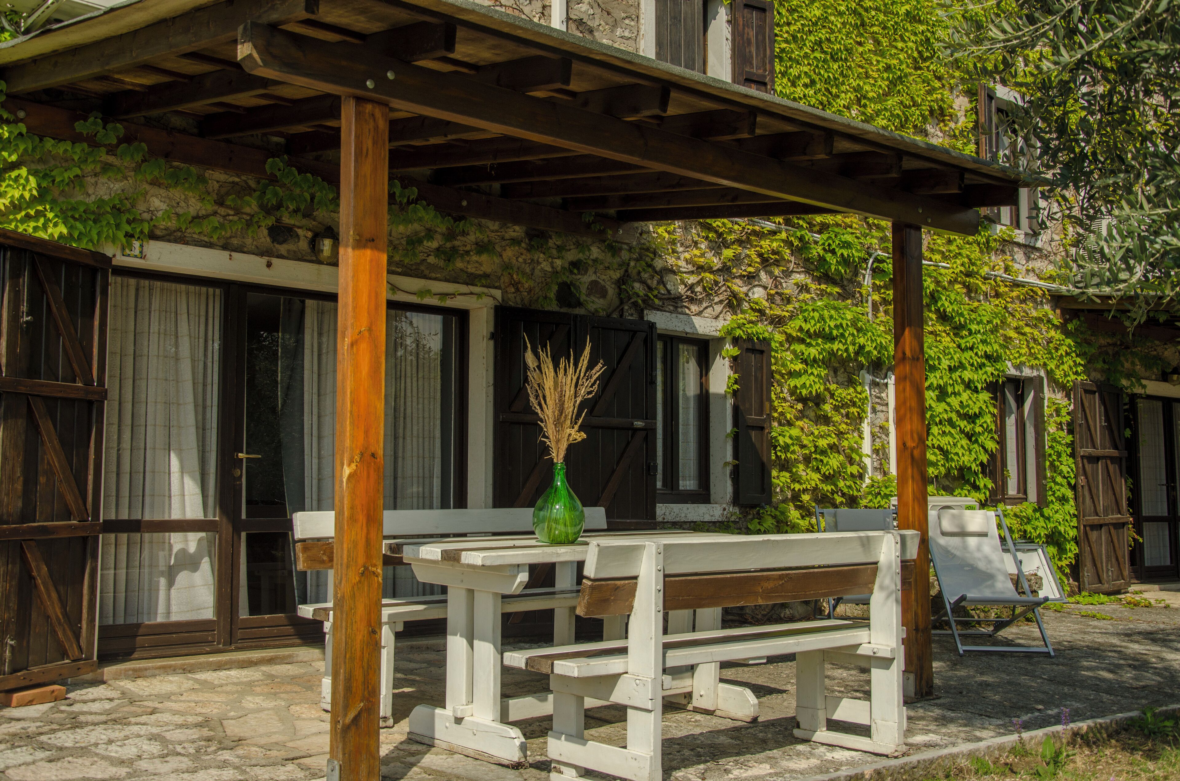 A covered outdoor seating area with benches and a table, surrounded by stone walls and greenery.