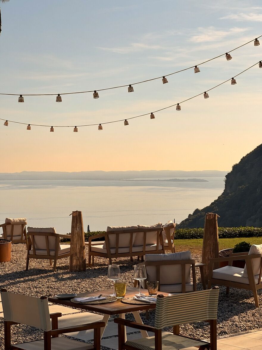 An outdoor seating area with chairs and tables, overlooking a body of water and a mountainous landscape.