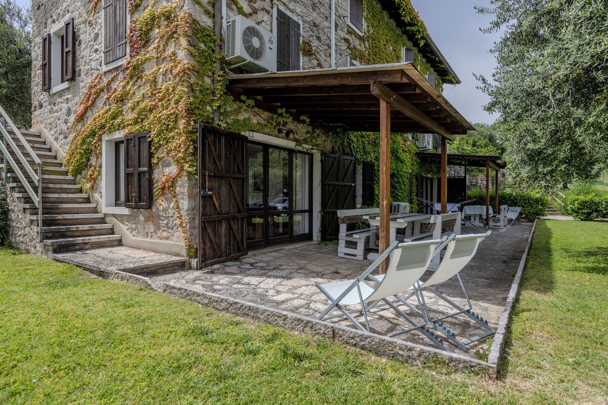 Un edificio de piedra con un patio cubierto, asientos al aire libre y una escalera que conduce a la entrada.