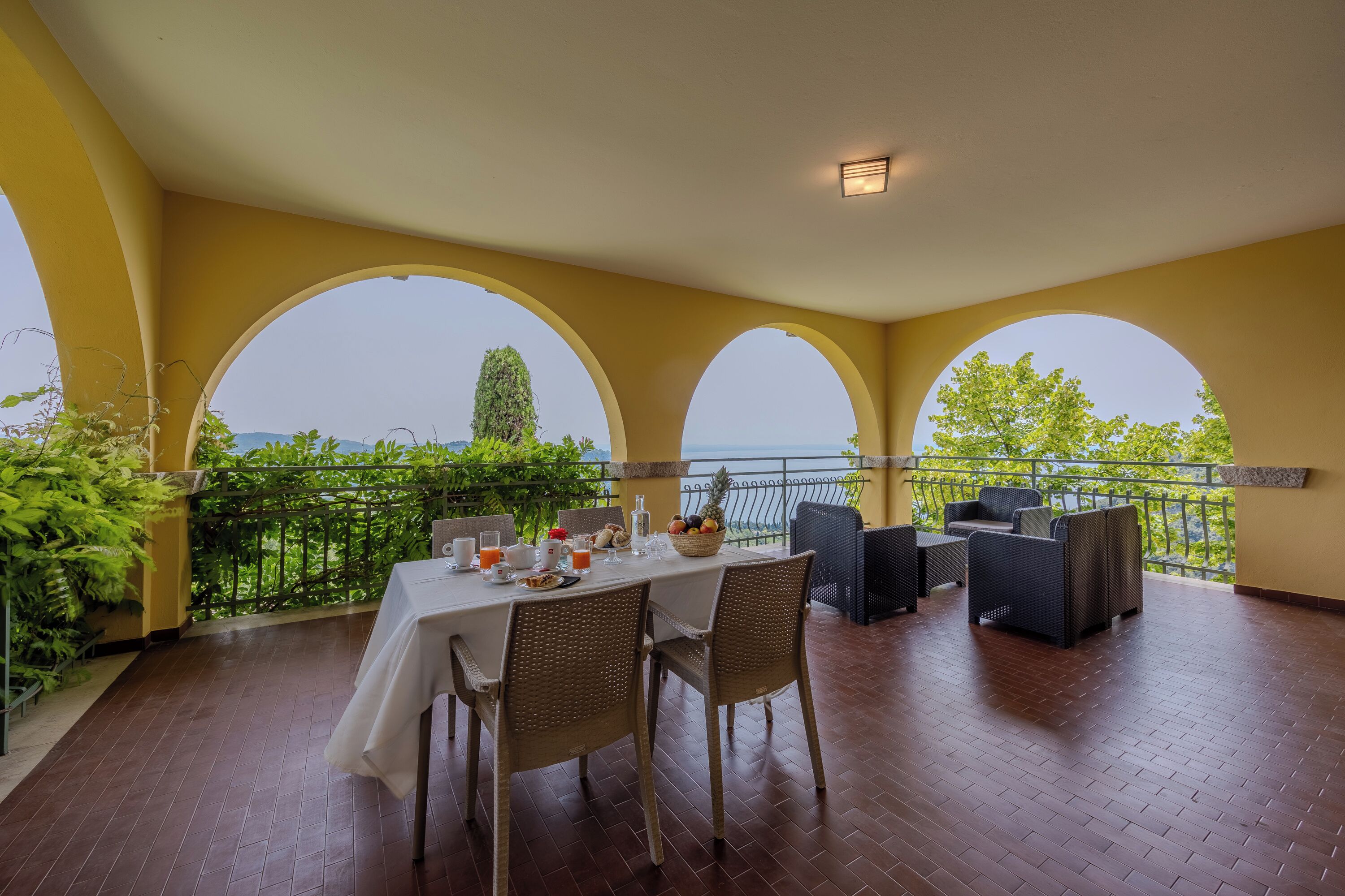 Un coin repas avec une table dressée pour le petit-déjeuner, entouré de chaises en osier, donnant sur un paysage pittoresque et agrémenté d’une balustrade.