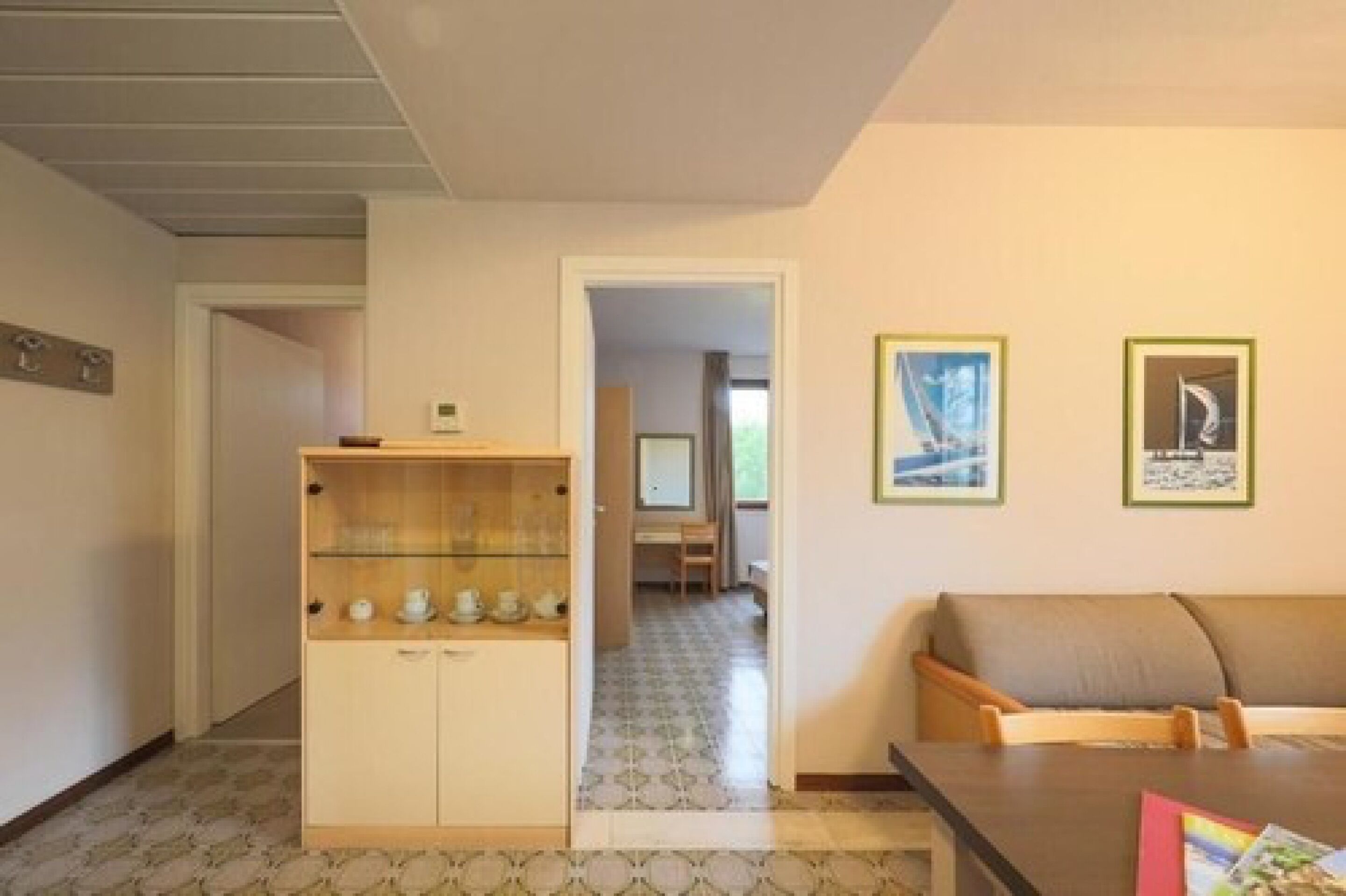 A room with a sofa, a wooden cabinet with cups, and two framed pictures on the wall.