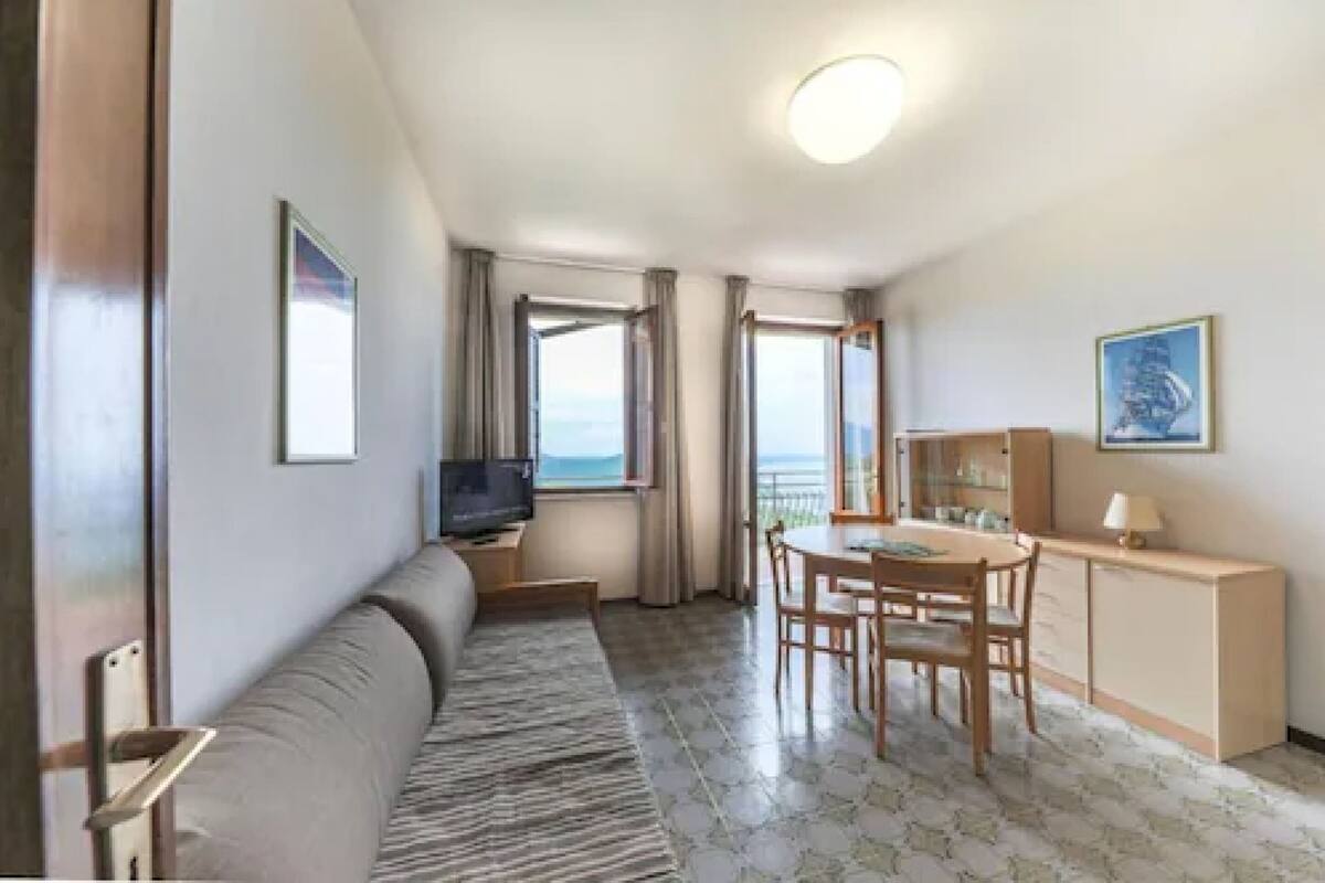 Hotellihuone, jossa on sohva, ruokapöytä tuoleineen, televisio ja parveke, jolta on näkymä merelle.