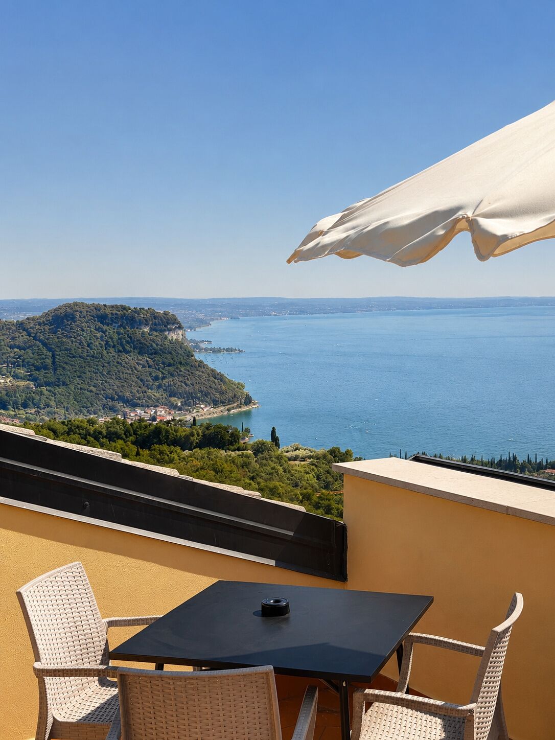A balcony with a table and chairs, overlooking a coastal landscape with a clear view of the sea and a distant island.