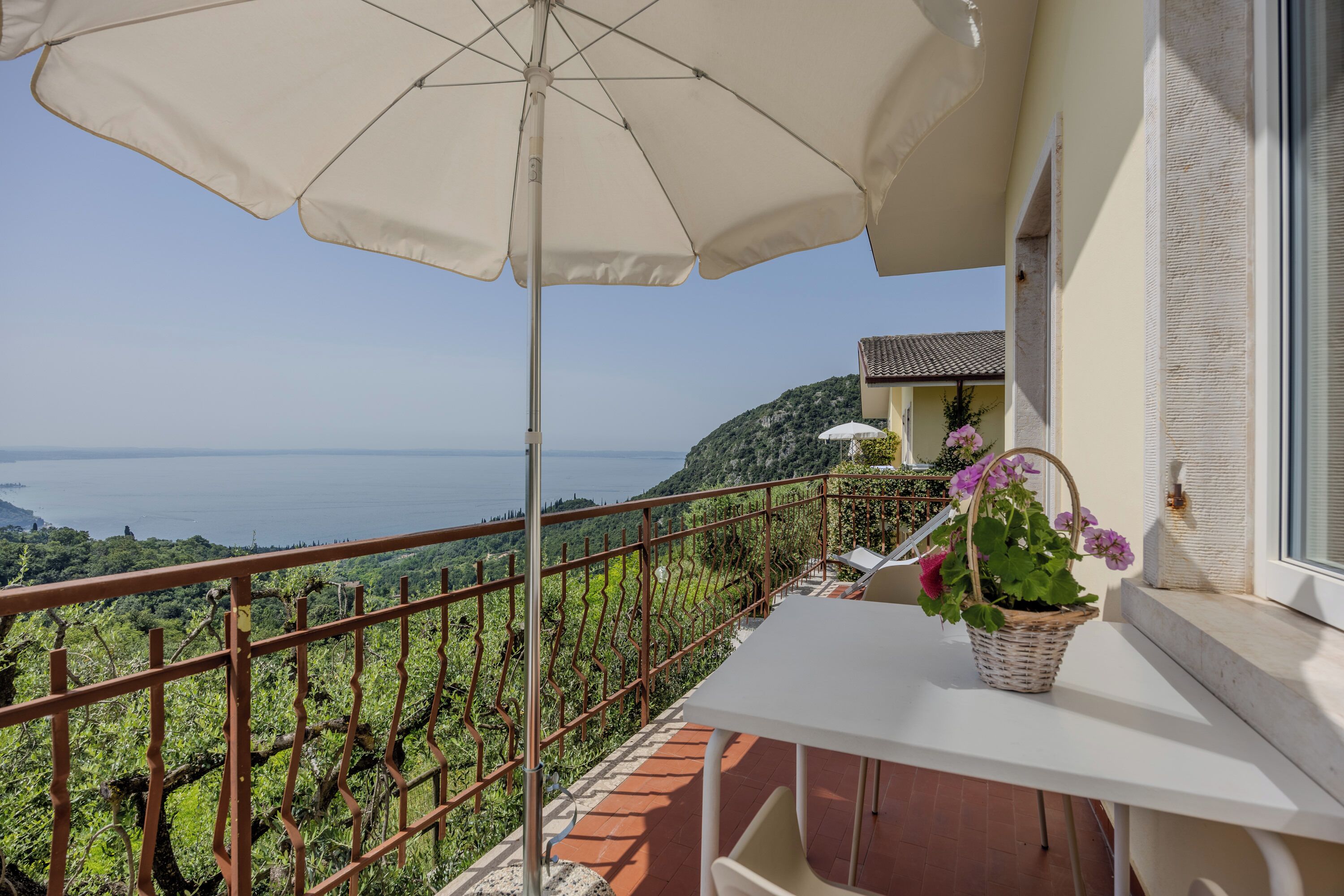 A balcony with a white table, a beige umbrella, and a wicker basket with flowers.