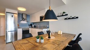 Une cuisine moderne avec une table à manger, des chaises, un luminaire suspendu et des étagères intégrées ornées de plantes.