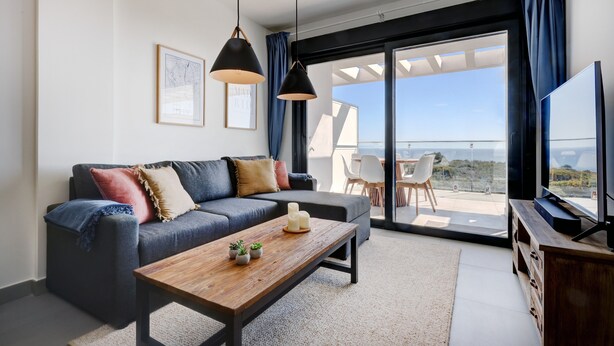 Un salon moderne comprenant un canapé, une table basse et un téléviseur, avec une grande porte-fenêtre coulissante donnant sur un balcon.