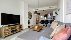 Un salon moderne doté d’un téléviseur à écran plat, d’un meuble de rangement en bois, d’un canapé gris, d’une table basse et de luminaires suspendus noirs.
