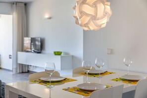 Une table à manger dressée avec des assiettes, des verres et des couverts, surmontée d’un luminaire suspendu au design moderne.