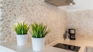 A kitchen with a stone backsplash, two potted plants, and a coffee maker. - 2-Bed Apartment in Miraflores with Pool, Terrace, Garden & Wi-Fi (Mijas)